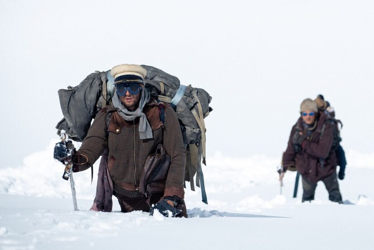 Muži nesoucí těžký náklad a putující zaboření ve sněhu ve filmu Sněžné bratrstvo.