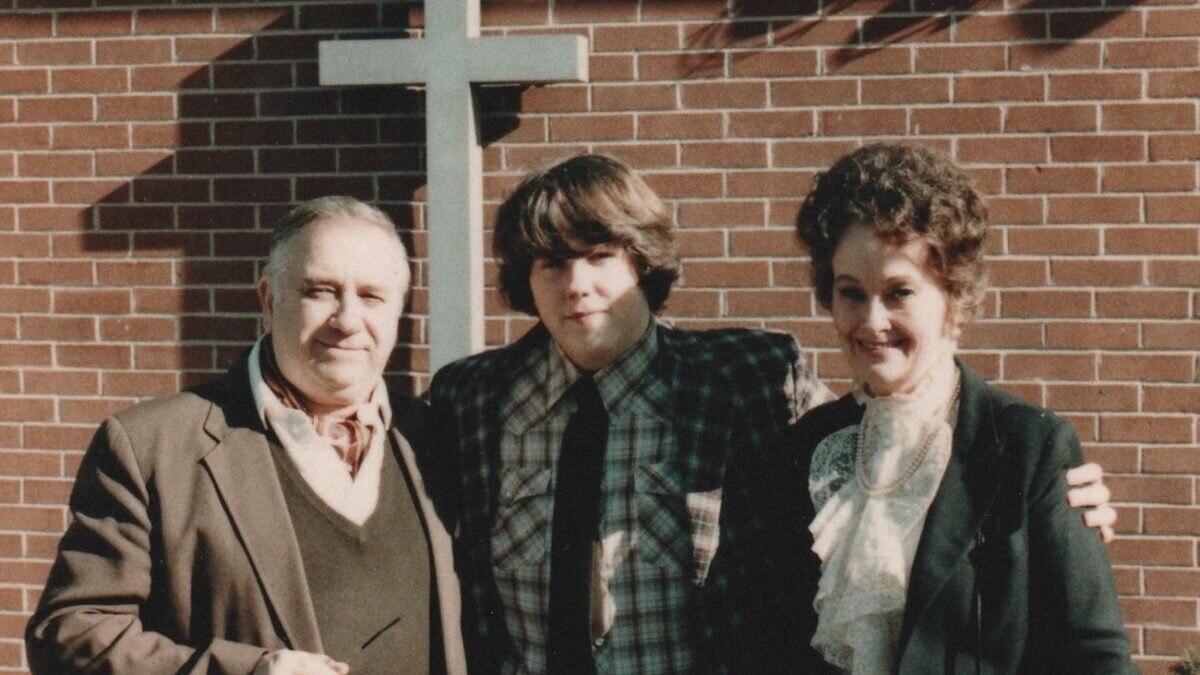Ed Warren, David Glatzel, a Lorraine Warren stojící před zdí s křížem.